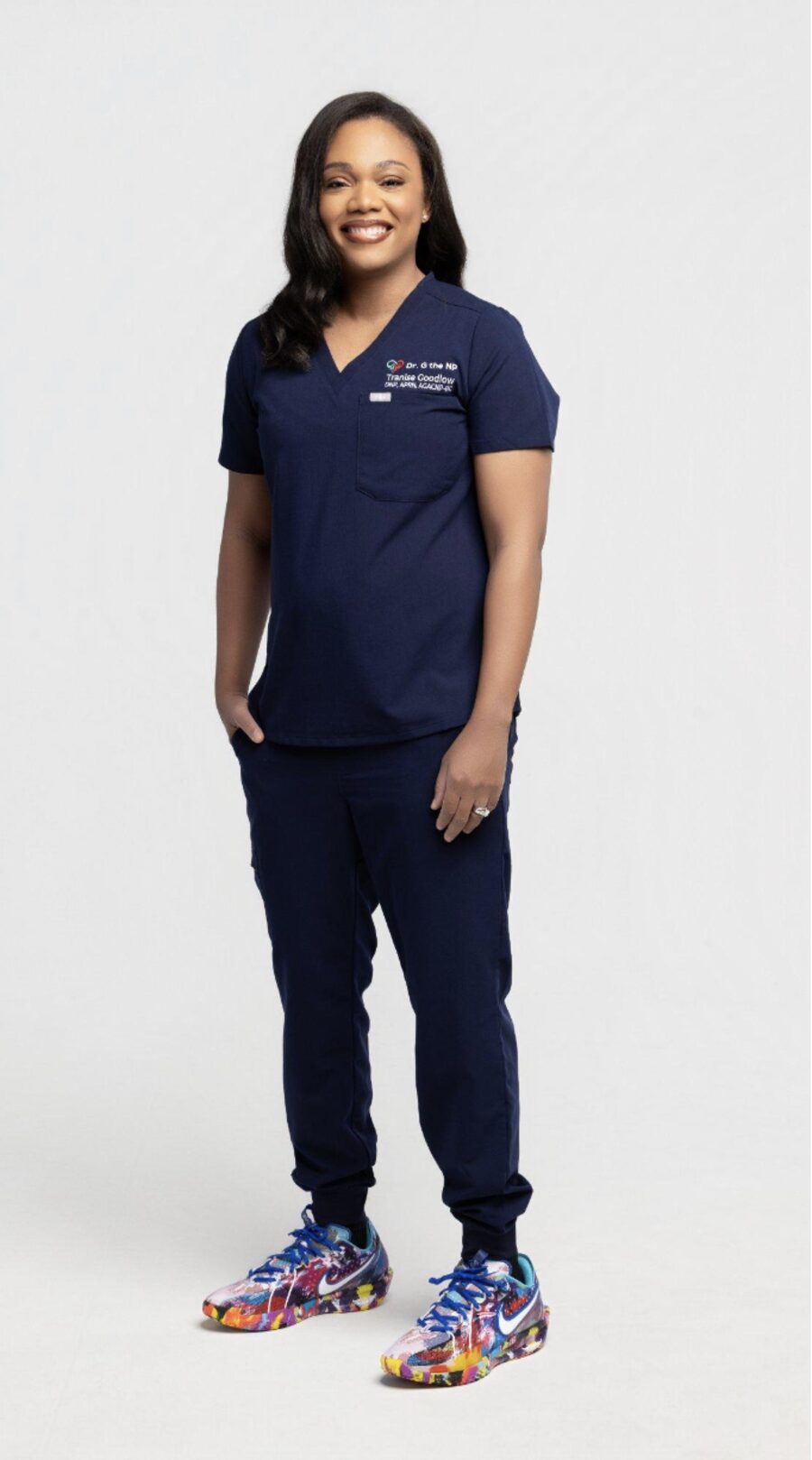 Dr. Tranise Goodlow standing in navy scrubs embroidered with the Dr. G the NP logo